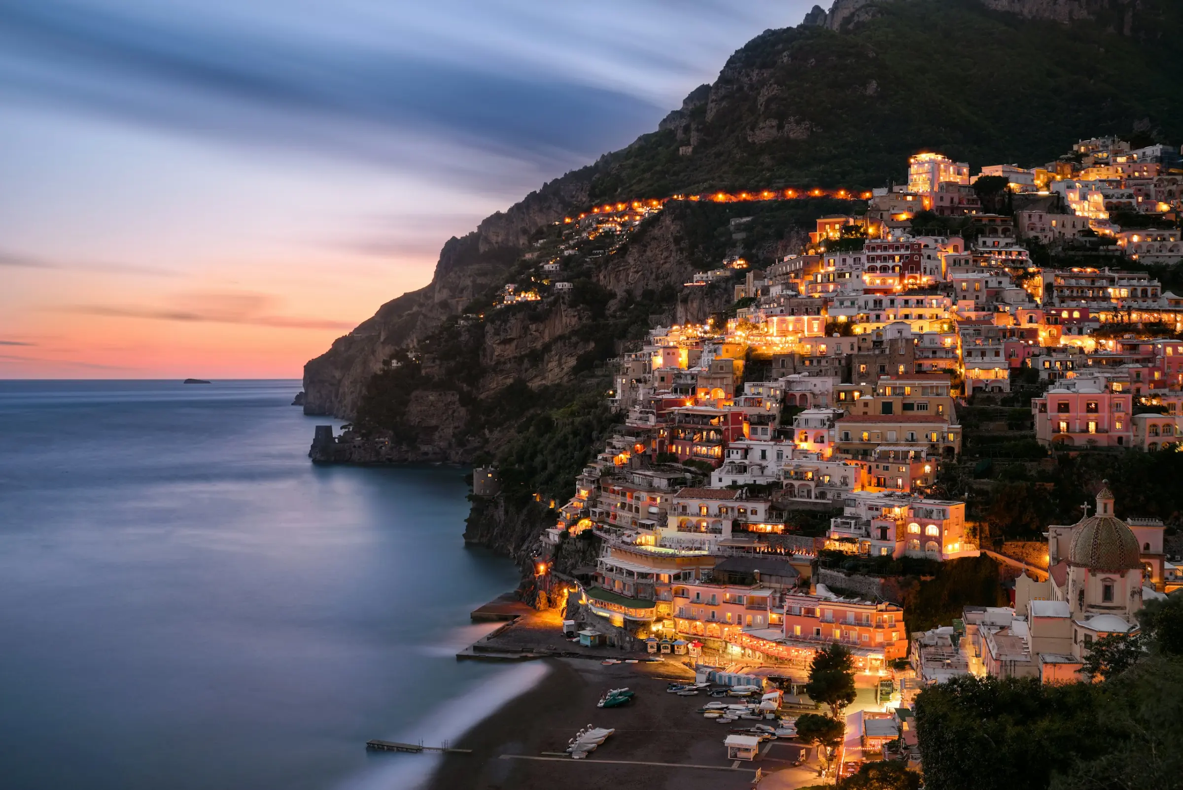 The cliffside village of Positano lit at dusk above the calm sea on Italy’s Amalfi Coast