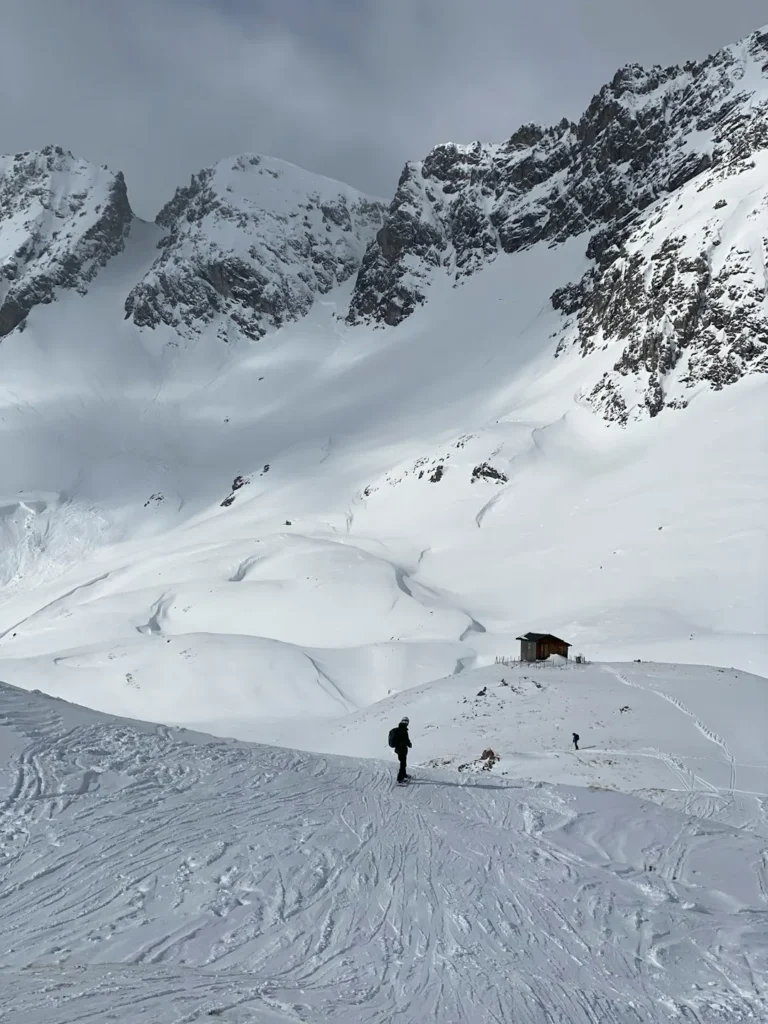 Skiers crossing a snow-covered alpine slope beneath rugged mountain peaks.