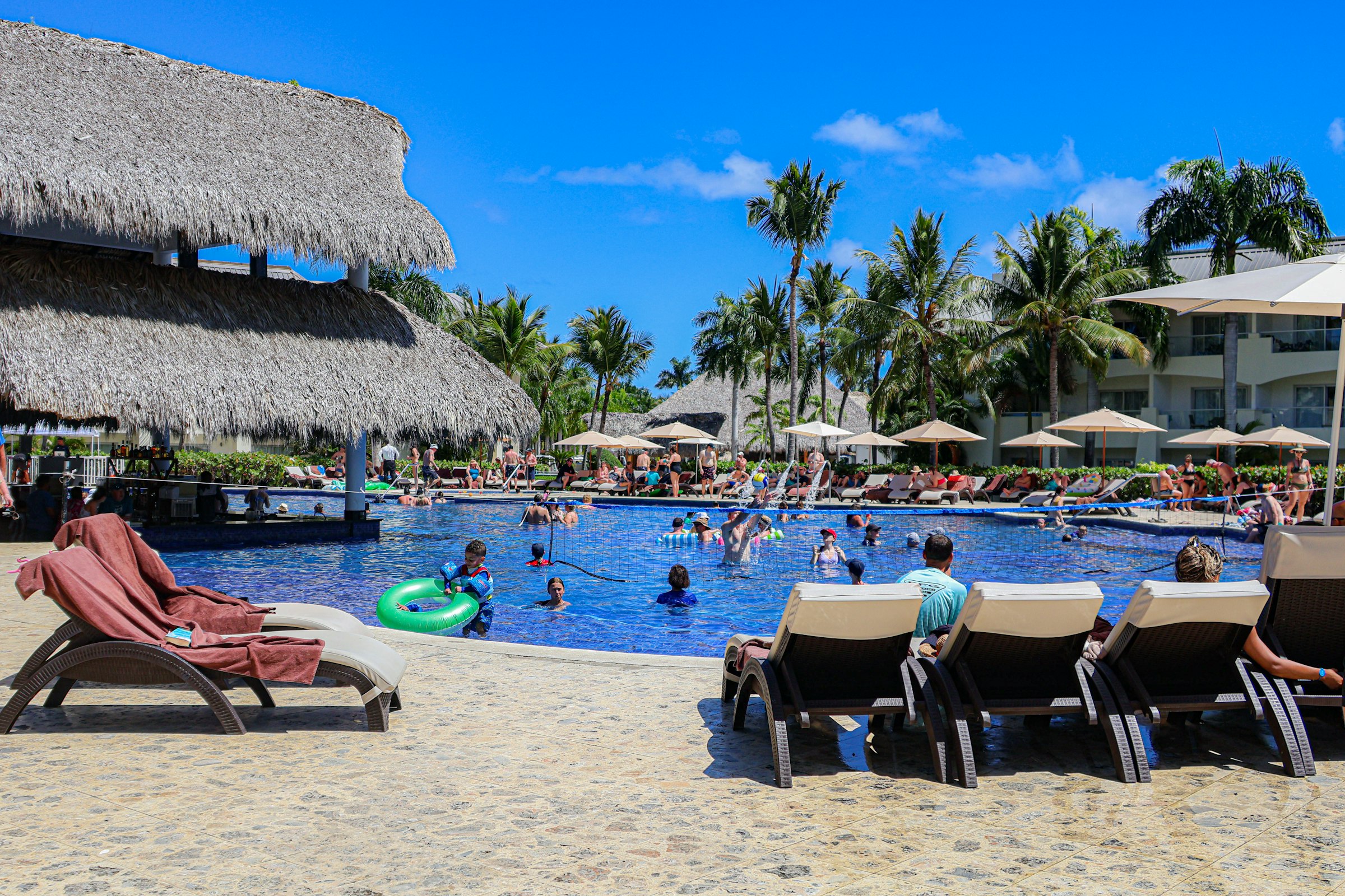 Travelers swimming and relaxing at a Caribbean resort pool with palm trees and a beach view
