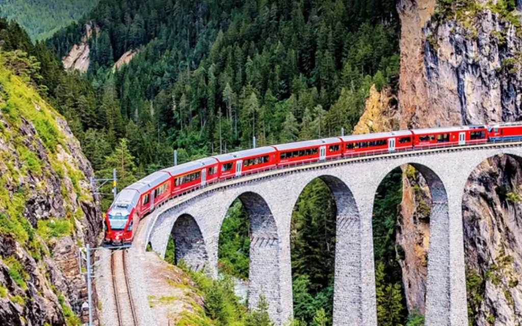 Red train crossing the stone Landwasser Viaduct through a forested gorge in Switzerland