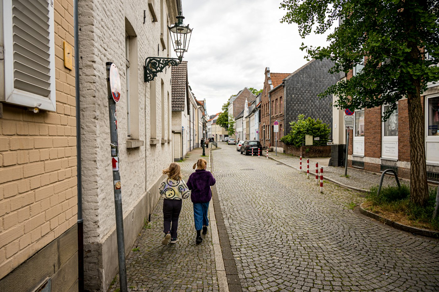 Two children walking down a cobblestone street between old European buildings